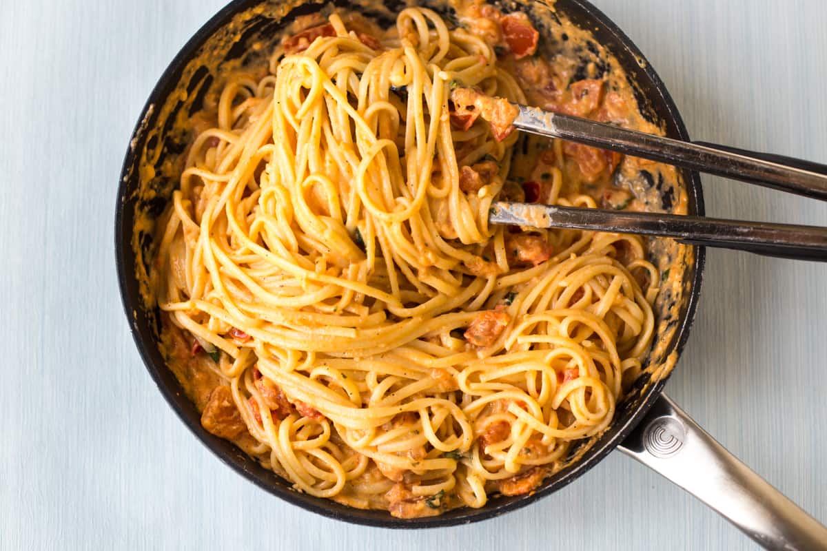 Linguine being tossed through tomato and mascarpone sauce in a frying pan.