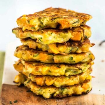 A stack of cheesy vegetable fritters on a board.