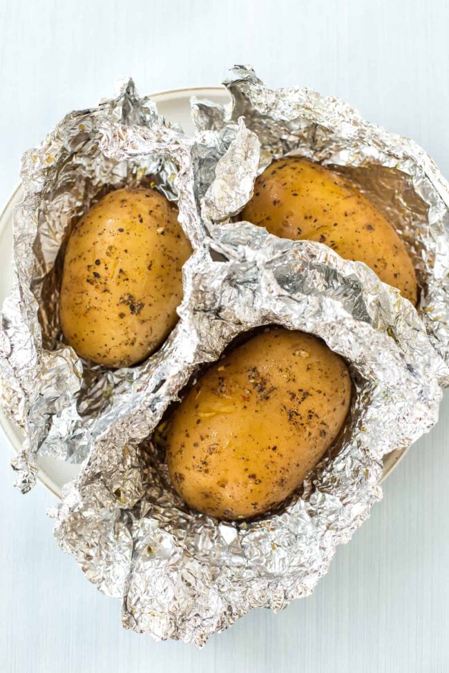 Three slow cooker baked potatoes in partially unwrapped foil.