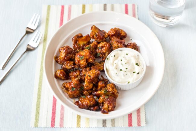 A bowlful of sticky cauliflower wings with a pot of sour cream dip on the side.