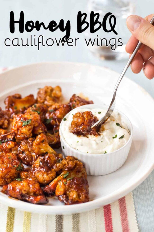A honey BBQ cauliflower wing on a fork, being dunked into a creamy dip.