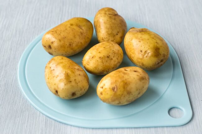 Raw potatoes on a blue chopping board.