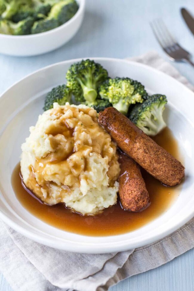 Sausage and mash in a bowl with broccoli and British-style gravy.