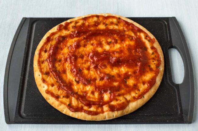 A shop-bought pizza base spread with tomato sauce.