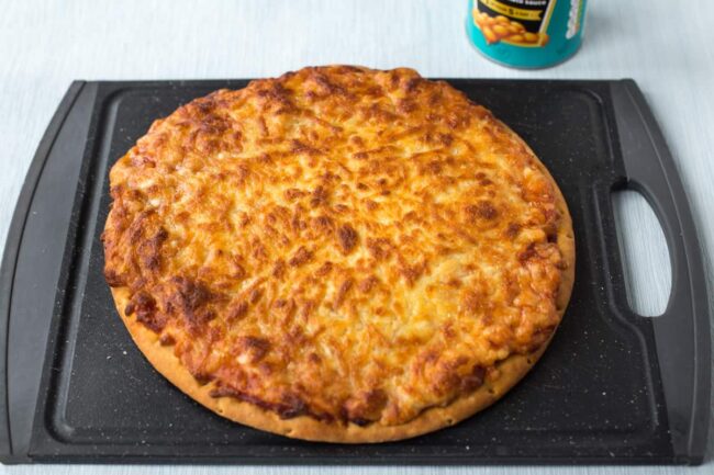 A crispy cheesy pizza on a black chopping board.