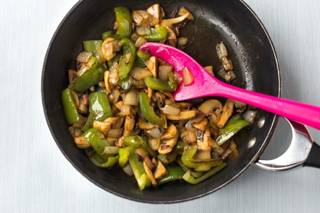 Onions, mushrooms and green peppers cooking in a frying pan.