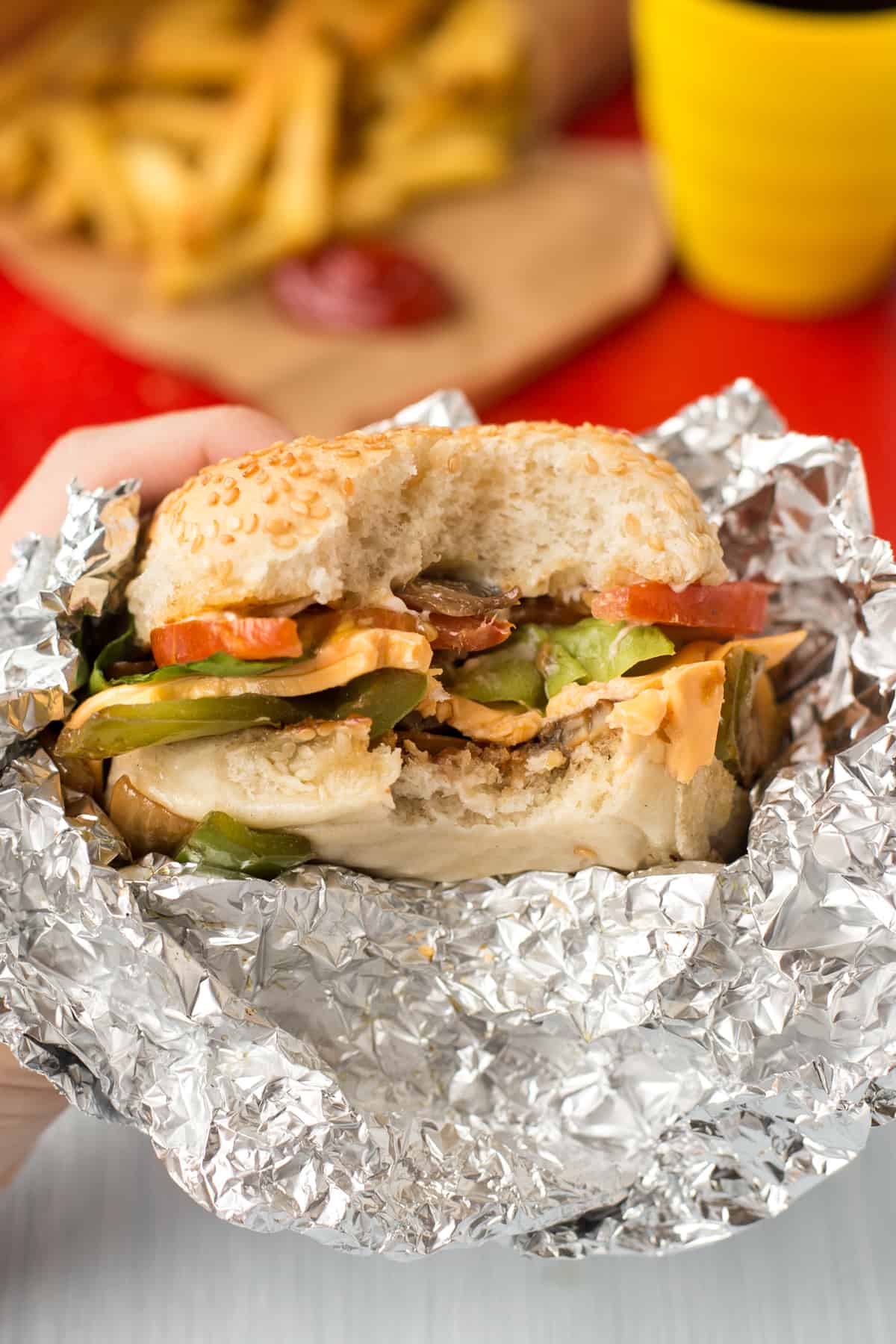 A hand holding up a homemade Five Guys cheese veggie sandwich with a bite taken.