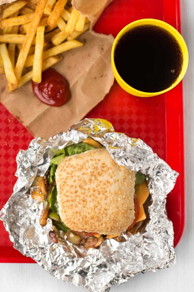 An aerial view of a homemade Five Guys burger and skin-on fries on a red fast food tray.
