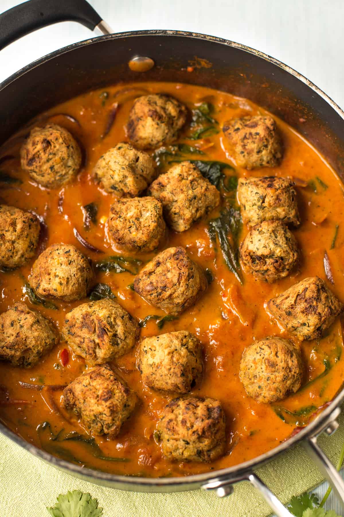 Crispy falafel sitting in a pan of curry sauce.
