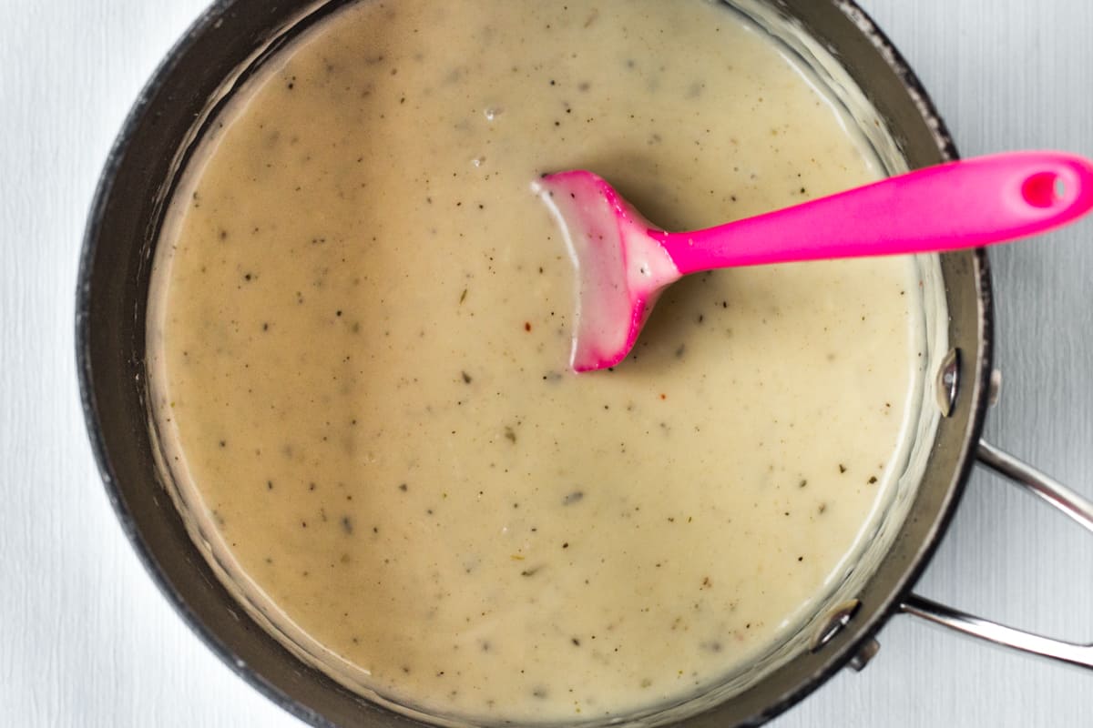 Cheese sauce cooking in a saucepan with a pink silicone spoon.