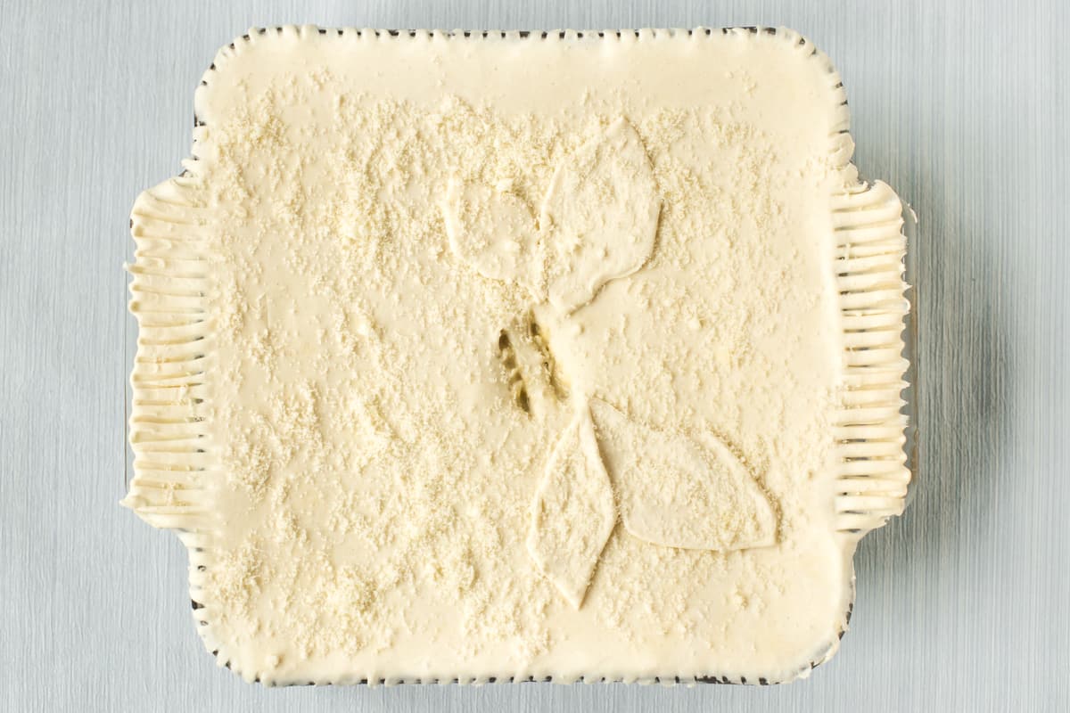 An uncooked vegetable pie with leaf shapes on top and crimped edges.