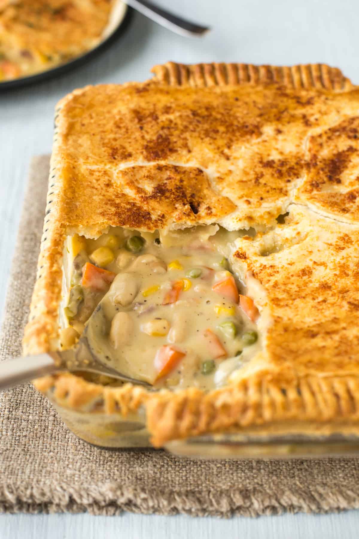 A puff pastry topped pie with cheesy vegetables showing underneath.