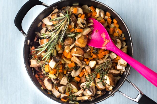 Mushrooms and carrots cooking in a frying pan with fresh rosemary and thyme.