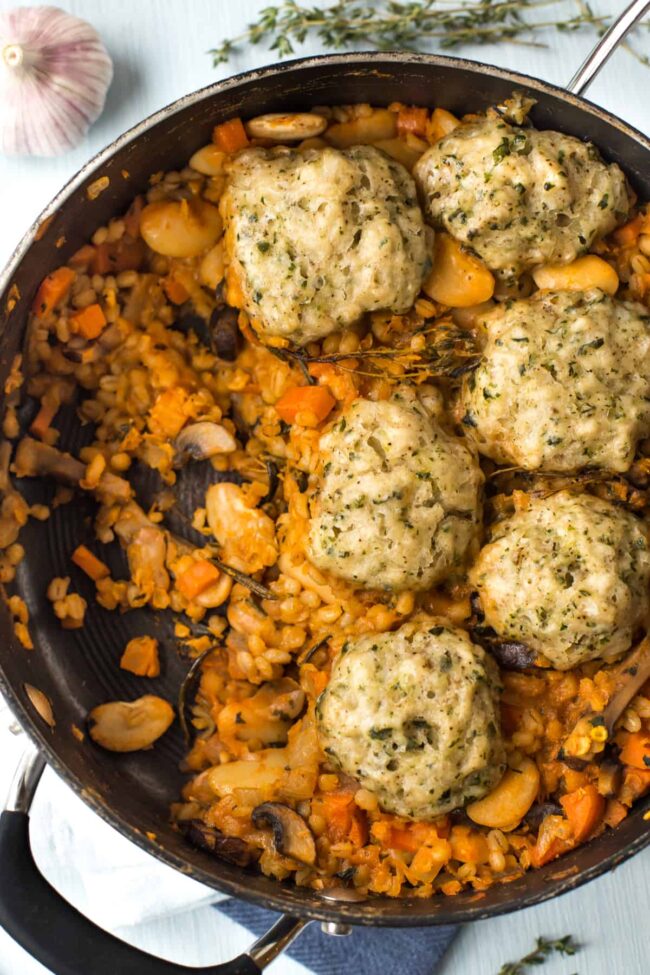 A pan full of vegan cassoulet topped with herby suet dumplings.
