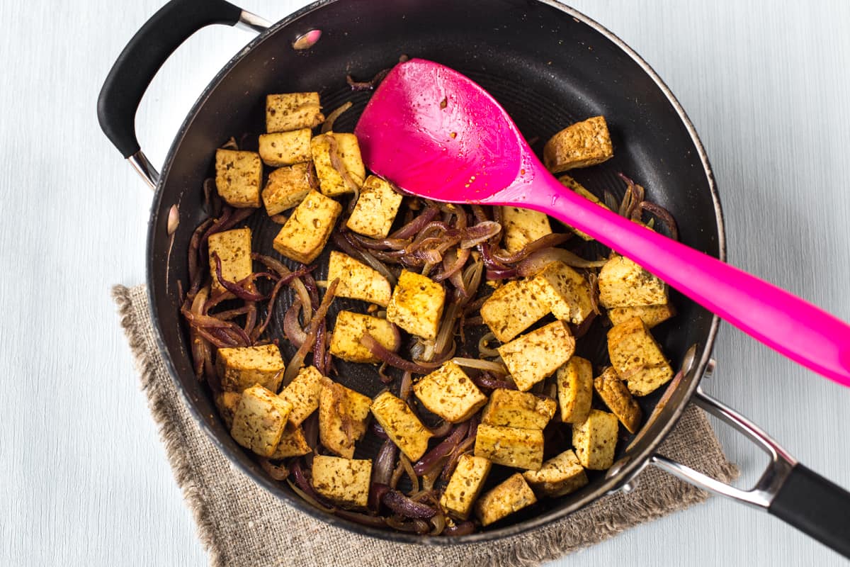 Smoked tofu and red onion cooking in a frying pan.
