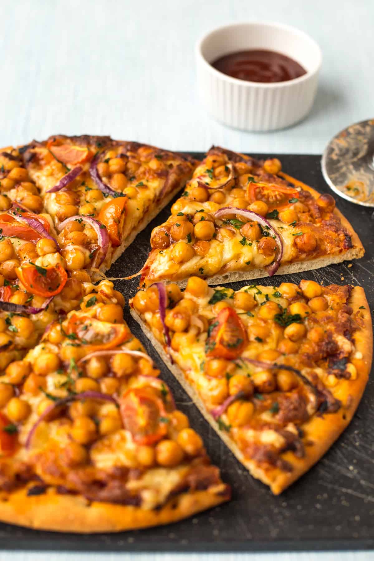 A BBQ chickpea pizza cut into slices on a board.
