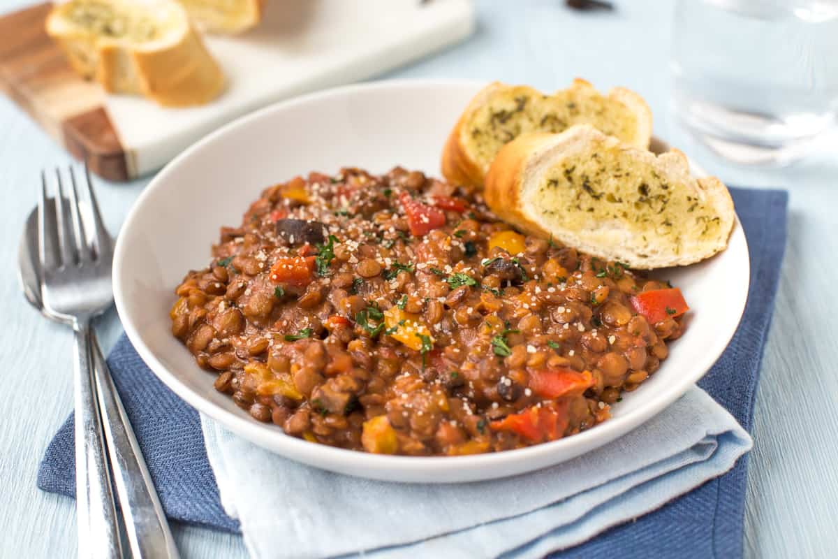 A portion of cheesy slow cooker lentils in a bowl with garlic bread.