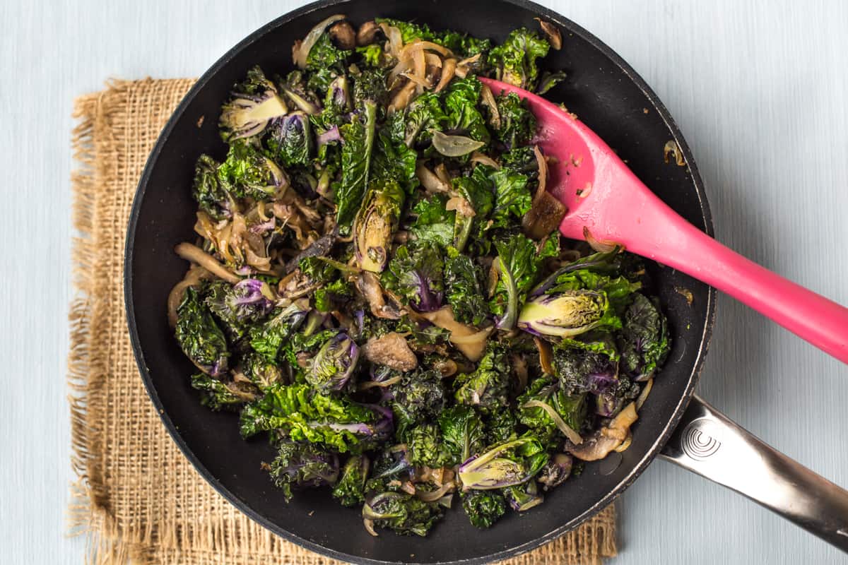 Sauteed kalettes, onions and mushrooms in a frying pan.