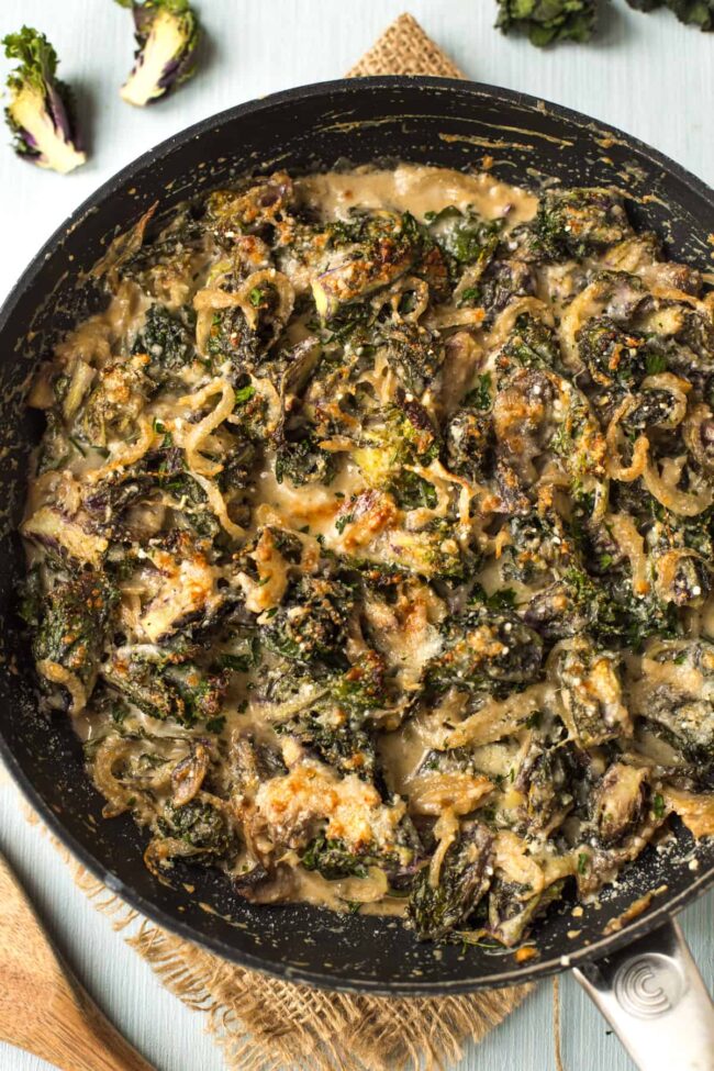 Creamed kalettes in a frying pan with a crispy, cheesy topping.