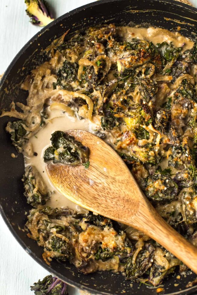 Creamed kalettes in a frying pan with a wooden spoon.
