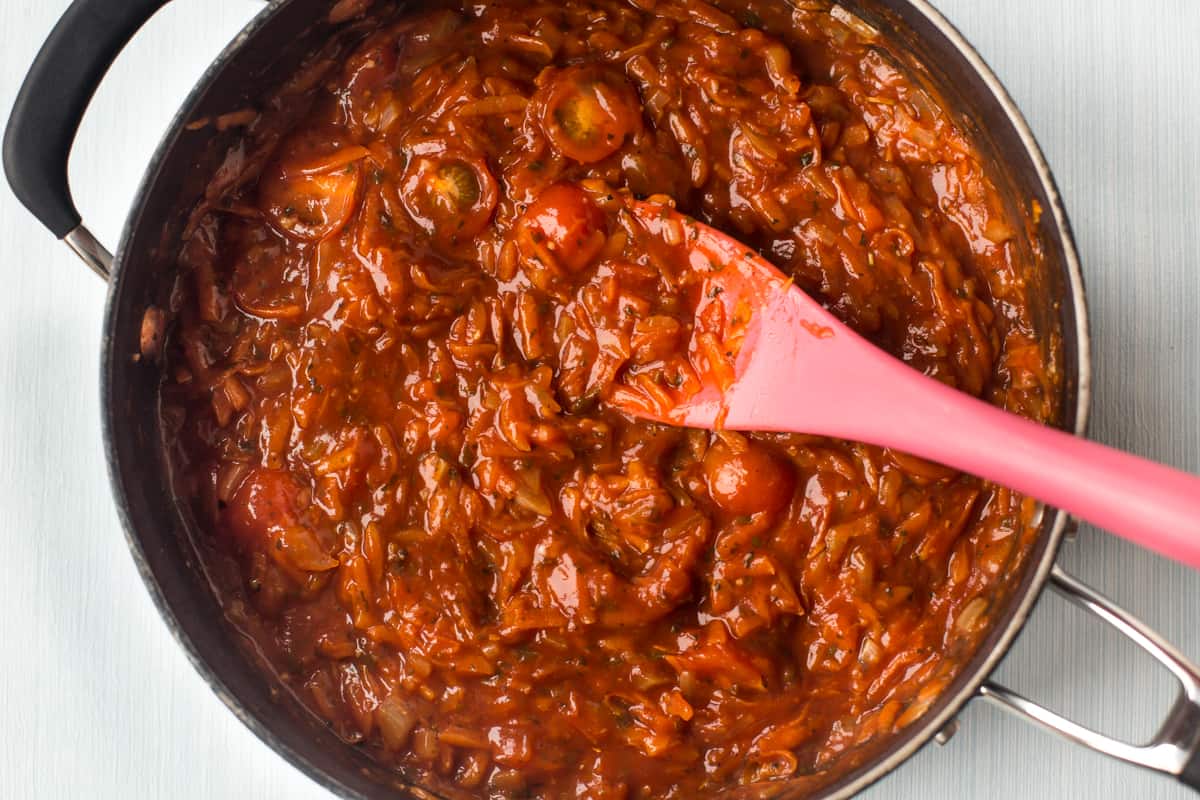 Homemade rich tomato sauce in a pan with a pink spoon.
