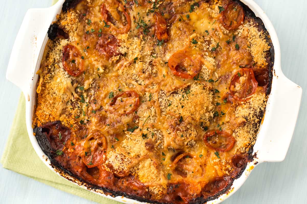 A tomato potato bake in a dish with a crispy breadcrumb and cheese topping.