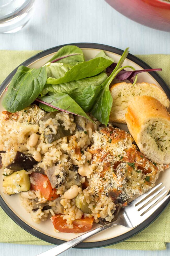 Portion of rice and vegetable casserole with garlic bread and salad.
