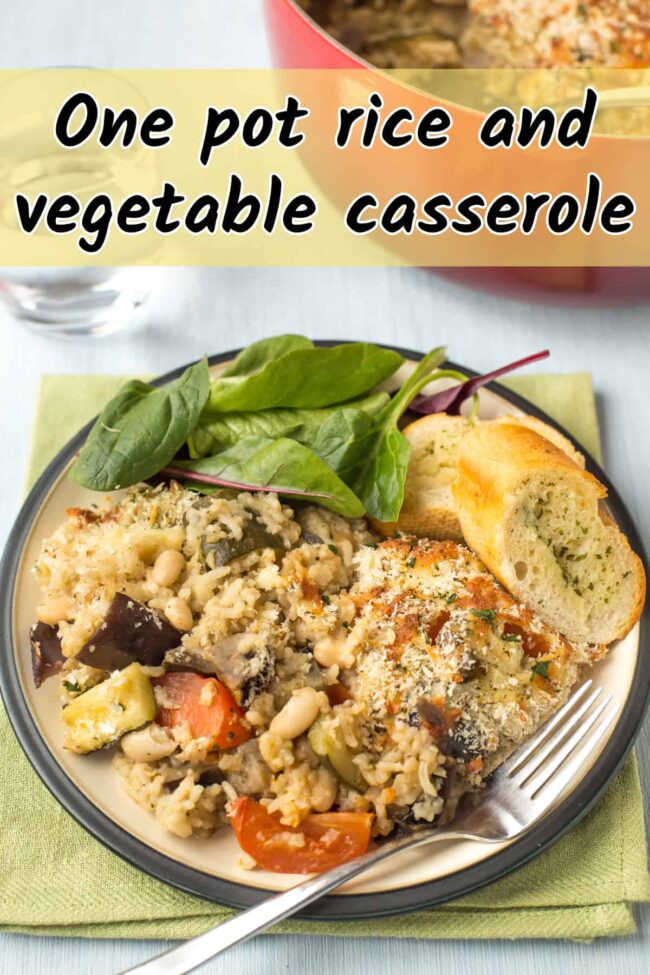 A portion of rice and vegetable casserole on a plate with salad and garlic bread.