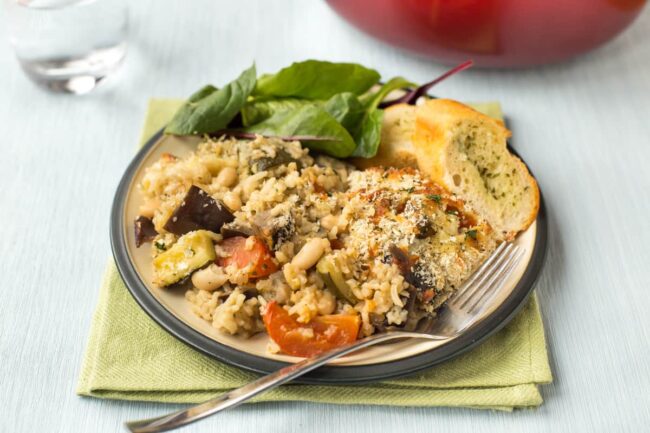 Portion of rice and vegetable casserole on a plate with garlic bread and salad.