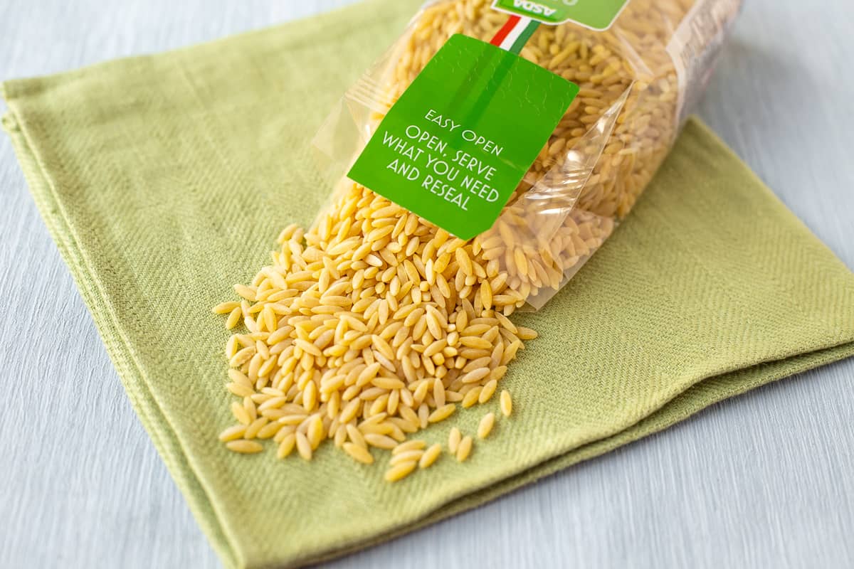 A packet of orzo spilling pasta onto a green linen.
