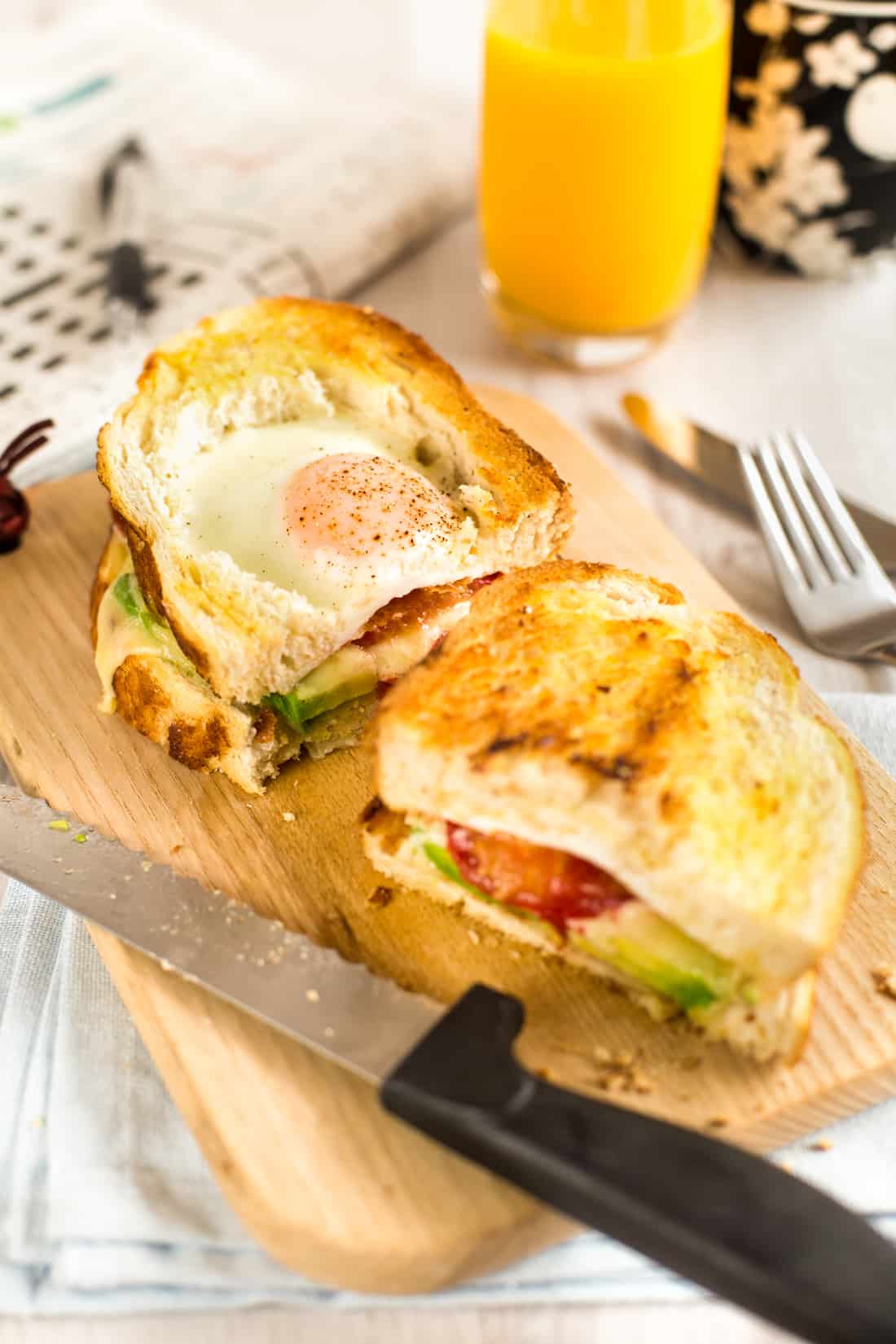 An egg in a hole breakfast sandwich cut in half on a board.