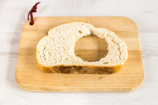 A slice of bread with a hole cut in it on a bread board.