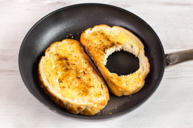 Crispy toast cooking in a frying pan, with a hole cut in one piece.