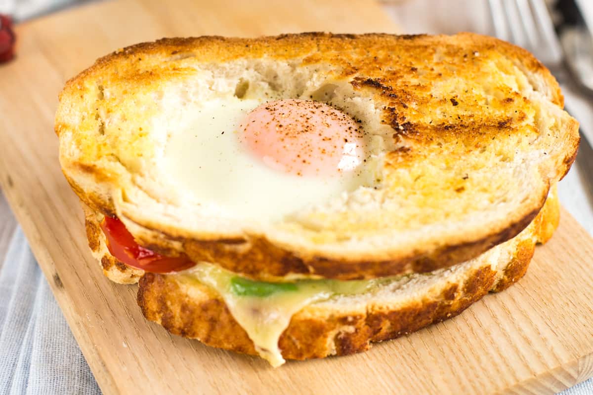 An egg in a hole breakfast sandwich with cheese melting out from the middle, and a gooey egg on top.