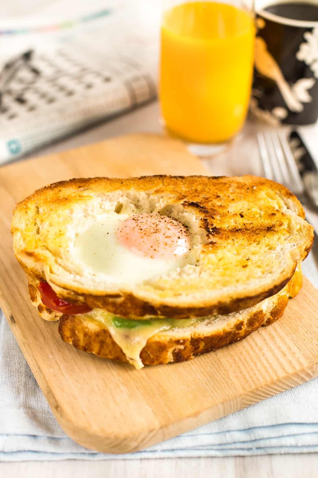 An egg in a hole breakfast sandwich with orange juice and coffee.