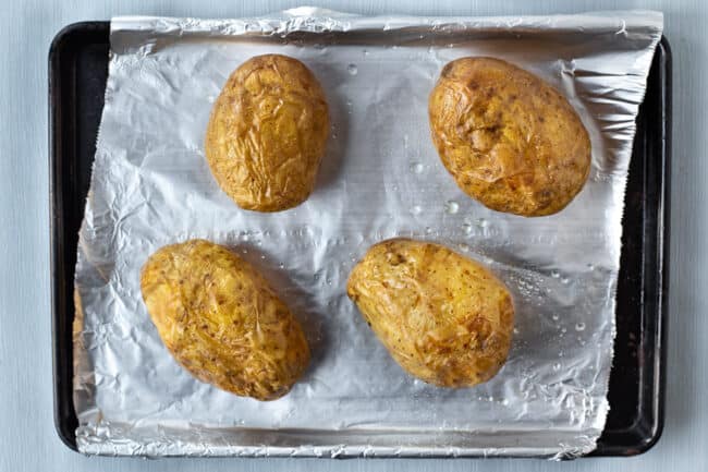 Crispy baked potatoes on a baking tray covered with foil.