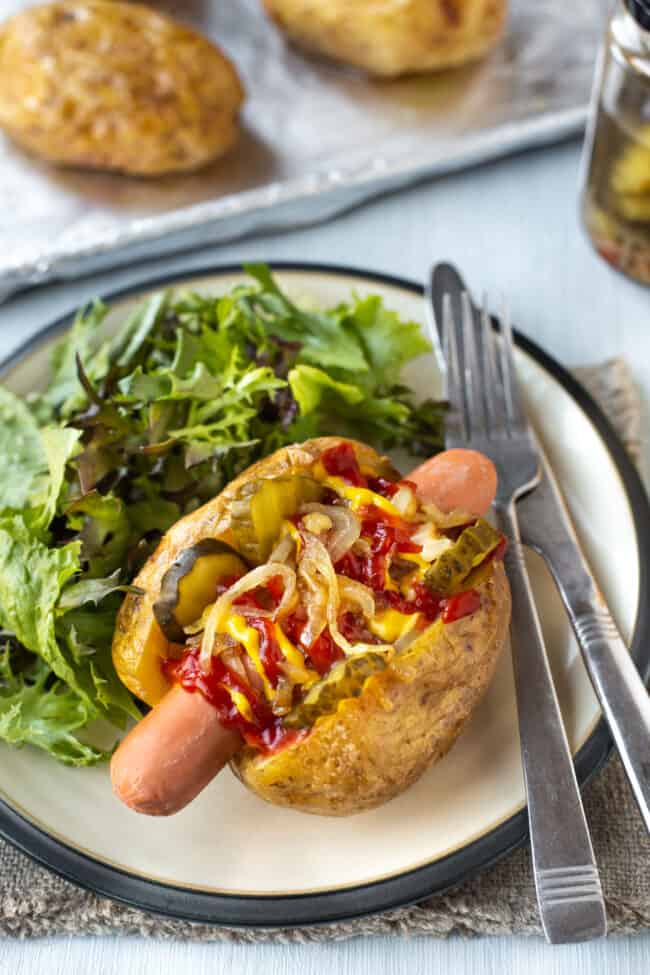 A hot dog baked potato topped with gherkins and fried onions.