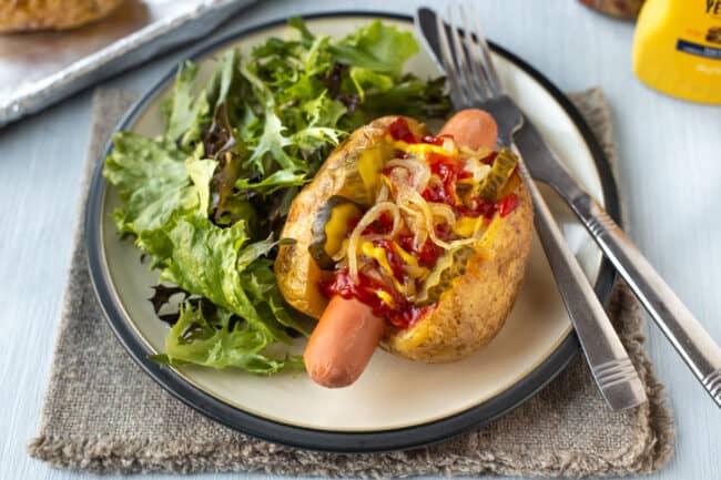 A hot dog jacket potato on a plate with salad.