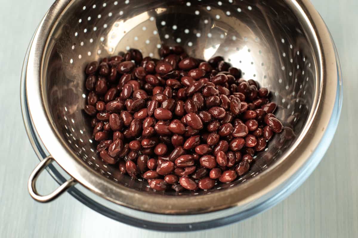 Tinned black beans draining in a metal sieve.