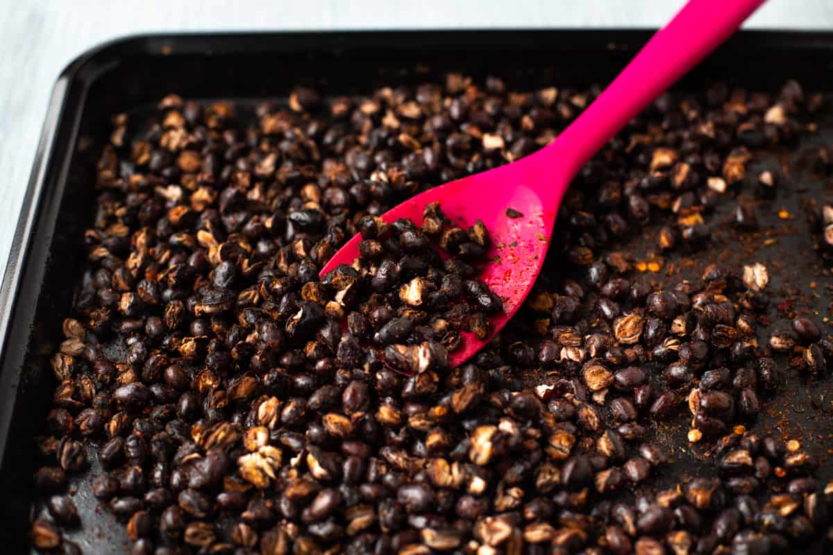 Roasted black beans on a baking tray with a pink spatula.
