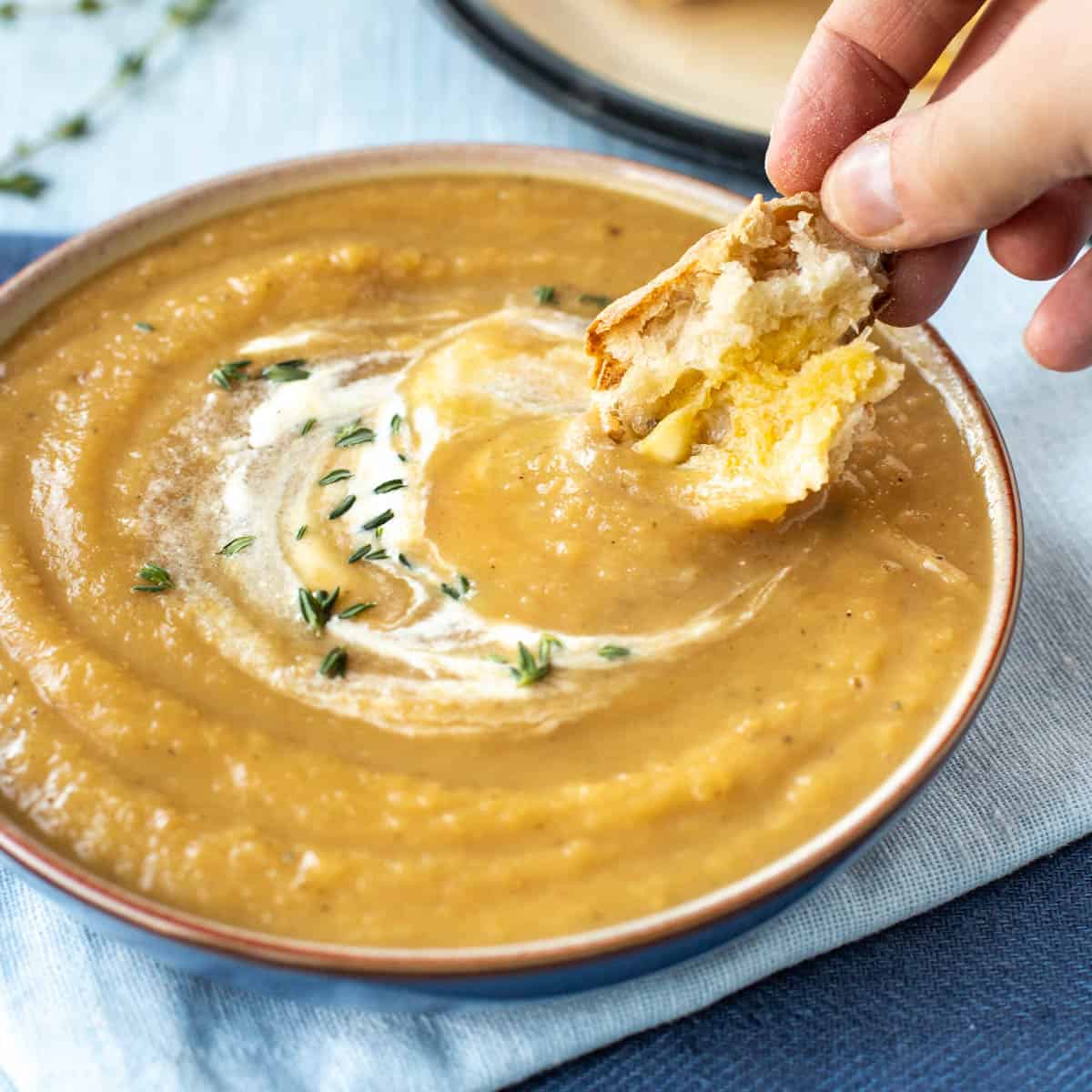 A hand dipping some crusty bread into a bowl of honey roasted parsnip soup.
