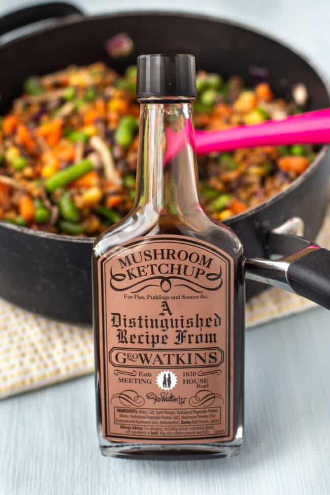 A bottle of mushroom ketchup propped up against a pan.