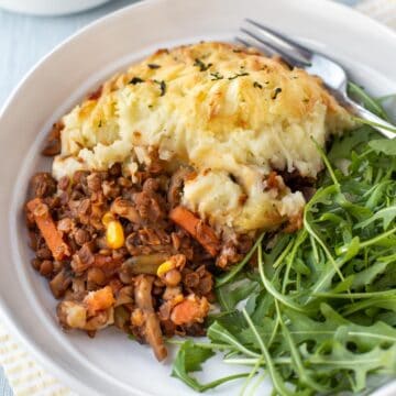 A portion of vegetarian shepherd's pie on a plate served with fresh arugula.