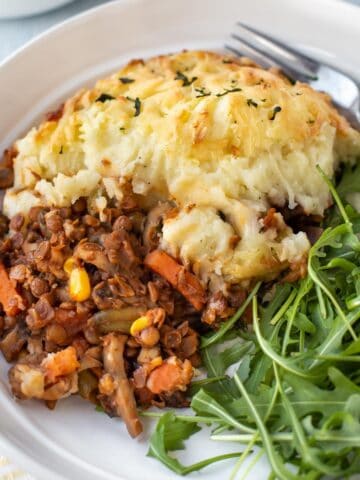 A portion of vegetarian shepherd's pie on a plate served with fresh arugula.
