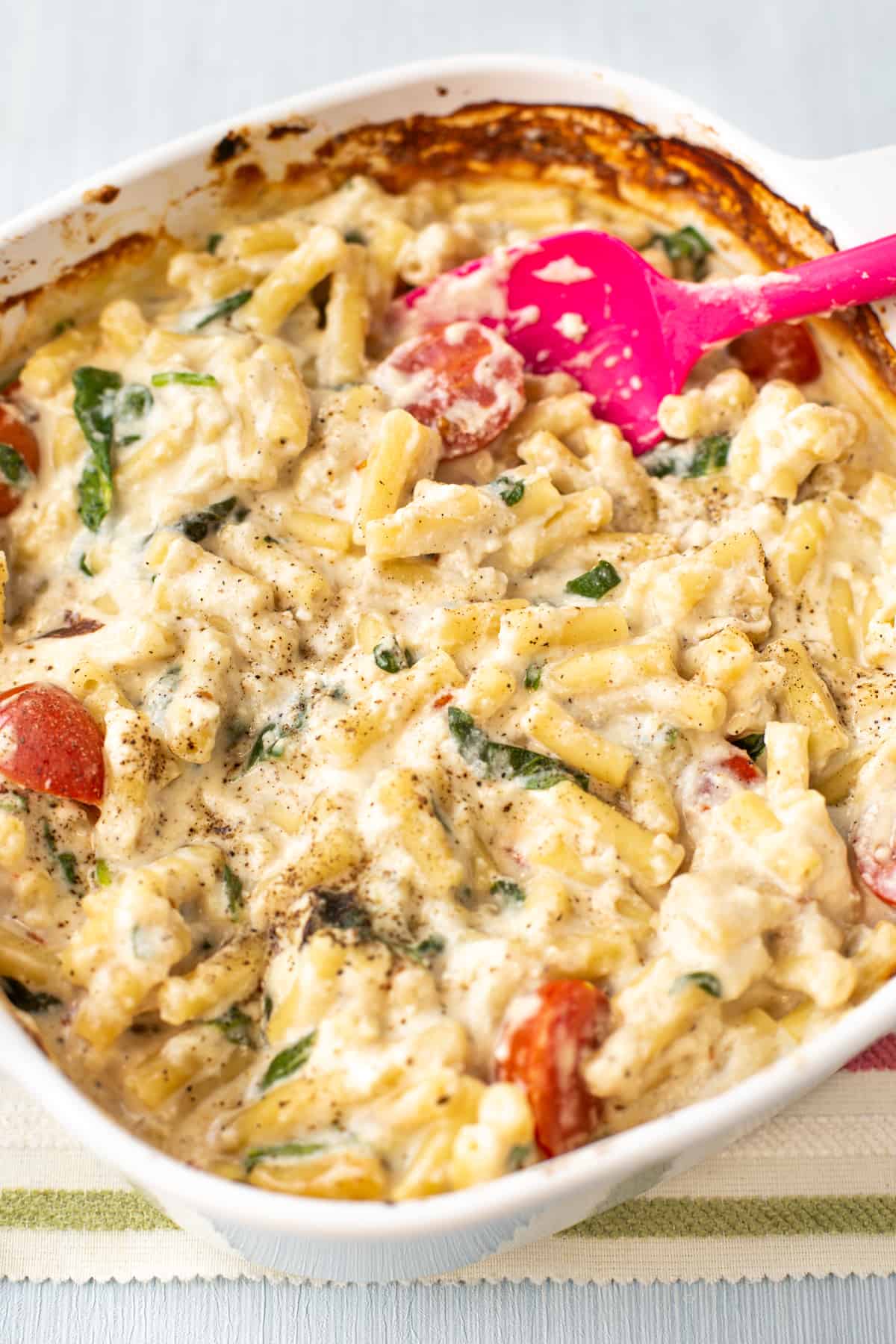 A baking dish full of cheesy pasta with spinach and tomatoes.