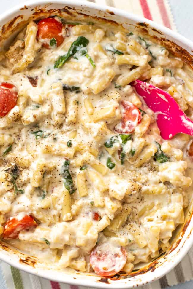A baking dish full of creamy feta mac and cheese with spinach and tomatoes.