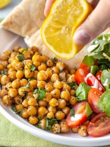 A hand squeezing lemon juice over some roasted chickpeas and salad.