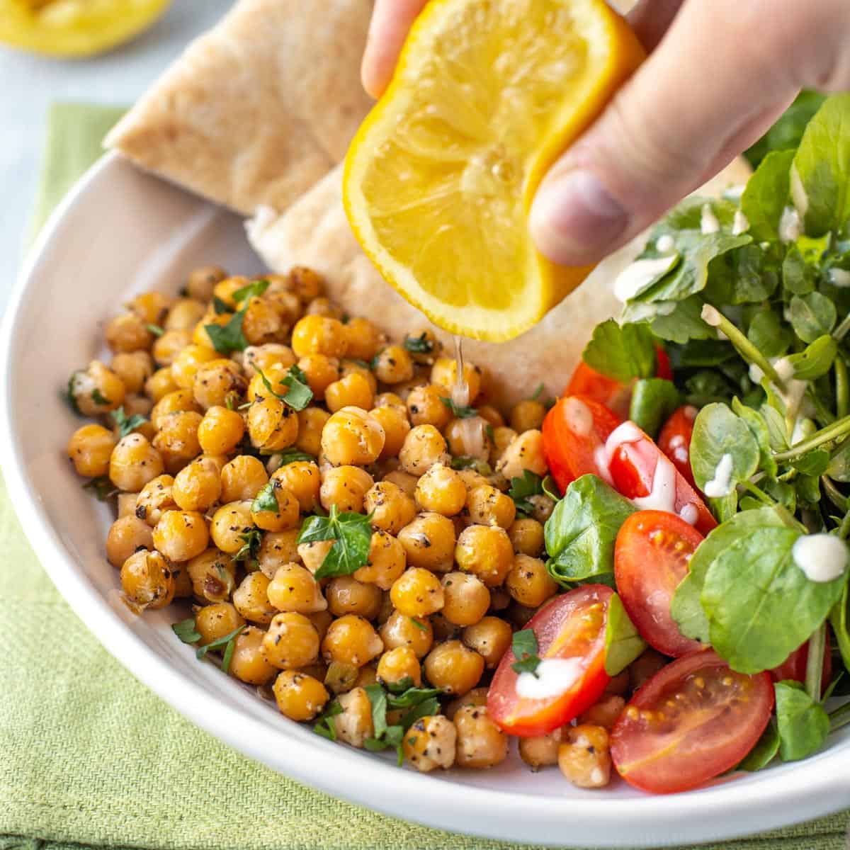 A hand squeezing lemon juice over some roasted chickpeas and salad.