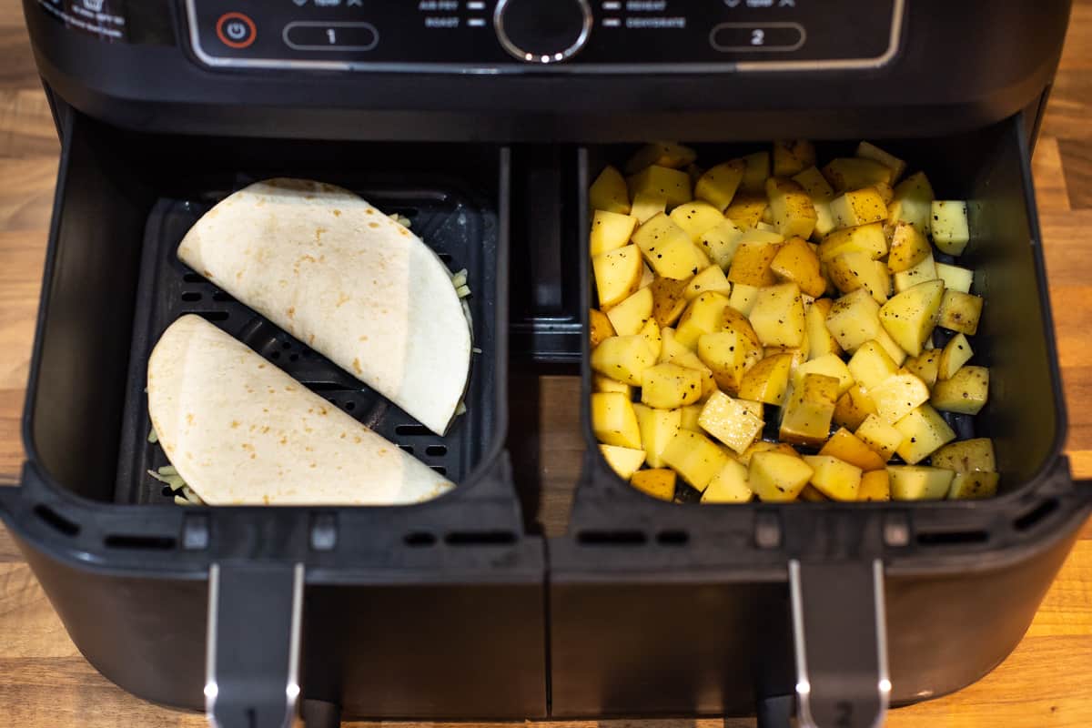 Uncooked quesadillas and diced potatoes in two air fryer baskets.