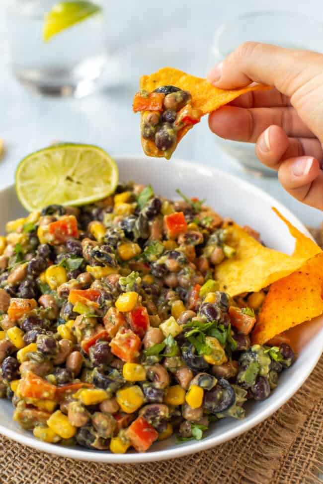 A hand holding up a tortilla chip with a scoop of creamy vegan cowboy caviar.